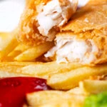 Close-up chip shop fried fish with crispy batter opened to show moist haddock.