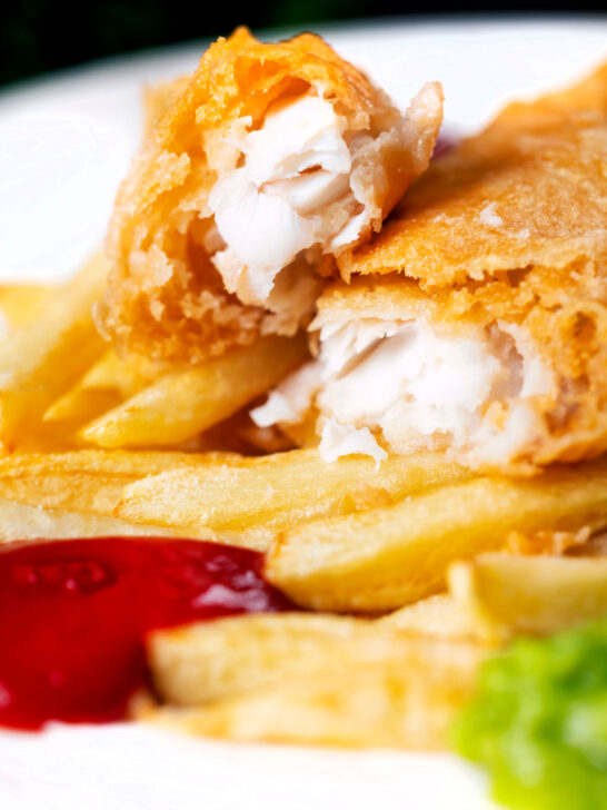 Close-up chip shop fried fish with crispy batter opened to show moist haddock.