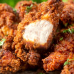 Close-up crispy fried spicy buttermilk chicken wings with a bite taken showing juicy meat.