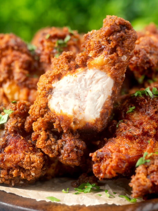 Close-up crispy fried spicy buttermilk chicken wings with a bite taken showing juicy meat.