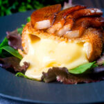 Couscous coated deep fried camembert cut open to show melted cheese, served with balsamic pears.