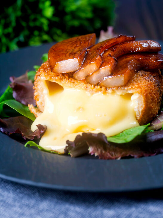 Couscous coated deep fried camembert cut open to show melted cheese, served with balsamic pears.