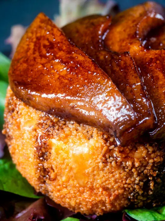 Close up balsamic glazed pears sat on couscous coated fried camembert cheese.