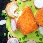 Overhead fried breaded goat cheese with sweet pea puree cut open showing the cheese.