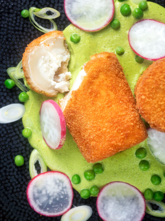 Overhead fried breaded goat cheese with sweet pea puree cut open showing the cheese.