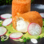 Fried breaded goat cheese with sweet pea puree cut open showing the semi melted cheese.