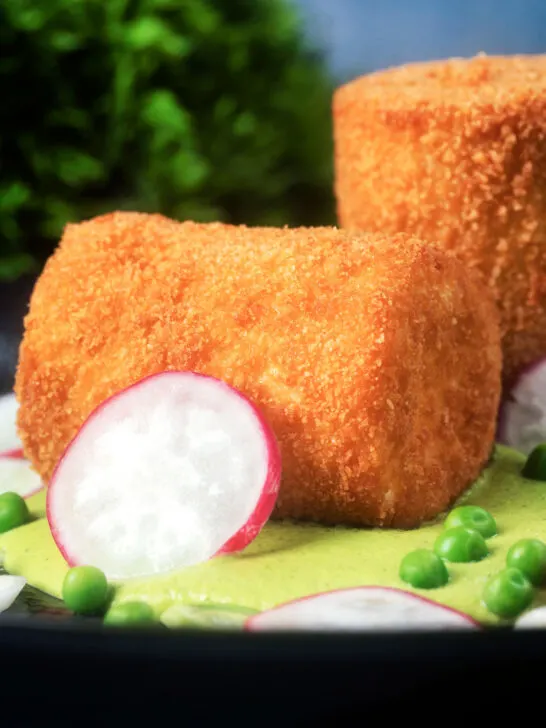 Close-up fried crumbed goat cheese with sweet pea puree, radishes and spring onions.