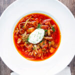 Overhead homemade borscht soup with beetroot, beef and cabbage served with sour cream.