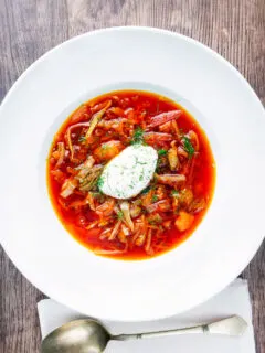 Overhead homemade borscht soup with beetroot, beef and cabbage served with sour cream.