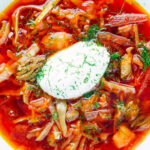 Overhead close-up homemade borscht soup with beetroot, beef and cabbage served with sour cream.