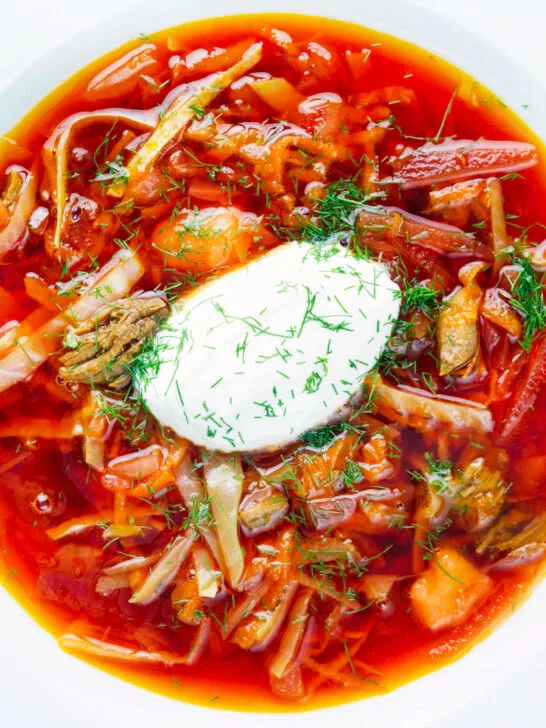 Overhead close-up homemade borscht soup with beetroot, beef and cabbage served with sour cream.