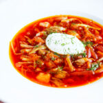 Homemade borscht soup with beetroot, beef and cabbage served with sour cream and dill.