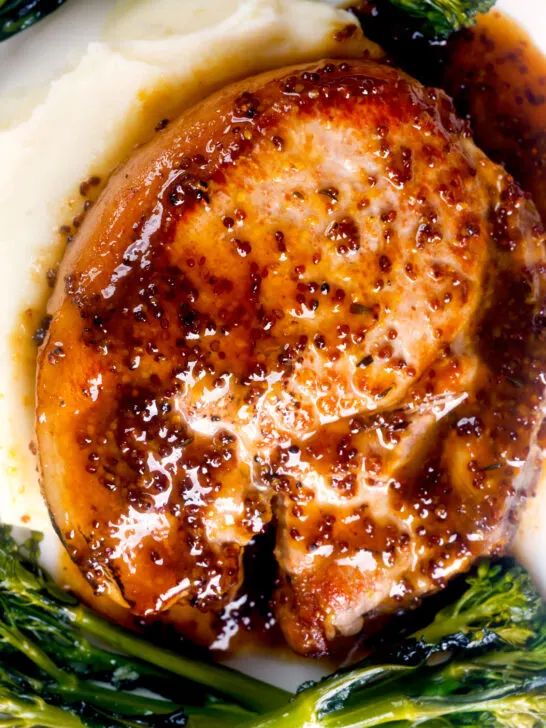 Overhead close-up thick cut honey mustard pork chops with roasted tenderstem broccoli and mashed potato.