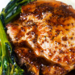 Close-up thick cut honey mustard pork chops with roasted tenderstem broccoli and mashed potato.