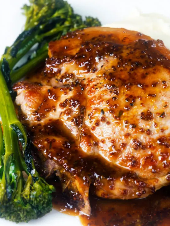 Close-up thick cut honey mustard pork chops with roasted tenderstem broccoli and mashed potato.