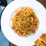 Overhead hot dog pasta topped with crispy onions and mustard breadcrumbs featuring a title overlay.