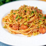 Hot dog spaghetti topped with crispy onions and mustard breadcrumbs featuring a title overlay.