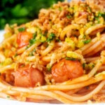 Close-up hot dog spaghetti topped with crispy onions and mustard breadcrumbs.