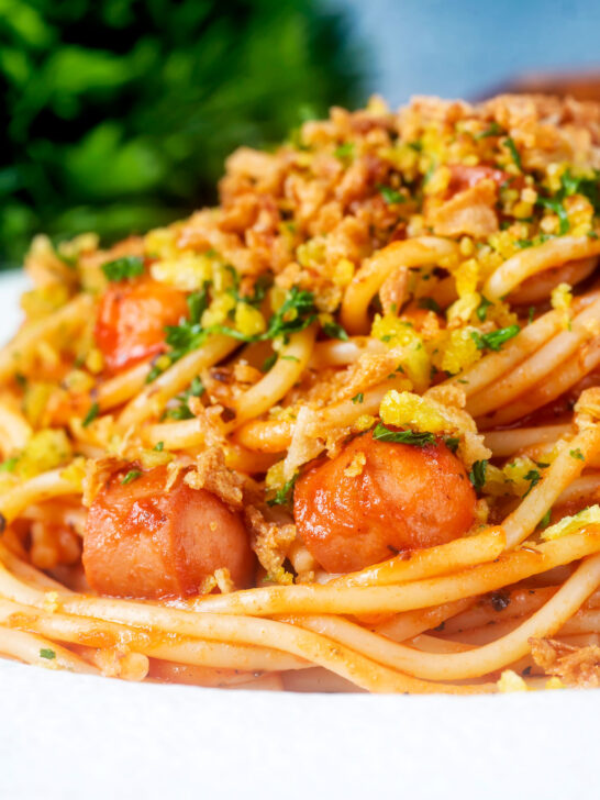 Close-up hot dog spaghetti topped with crispy onions and mustard breadcrumbs.