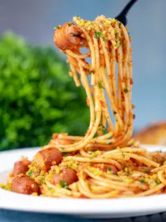 Hot dog pasta with a mustard and crispy onion crumb being eaten with a fork.