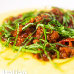 Close-up sausage ragu made with Italian sausages and tomatoes served with polenta featuring a title overlay.