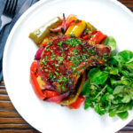 Overhead tray baked paprika pork chop with red wine and honey bell peppers and onions featuring a title overlay.