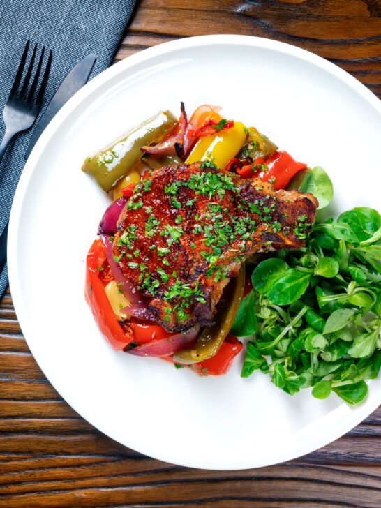 Overhead tray baked paprika pork chop with red wine and honey bell peppers and onions featuring a title overlay.