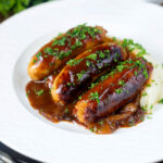 Slow cooker pork sausages in a mustard and BBQ sauce served with mashed potato featuring a title overlay.