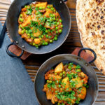 Overhead Indian aloo matar curry with potatoes and peas served with naan bread.