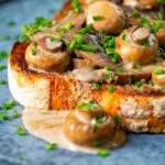 Close-up creamy garlic mushrooms on toast with snipped chives.