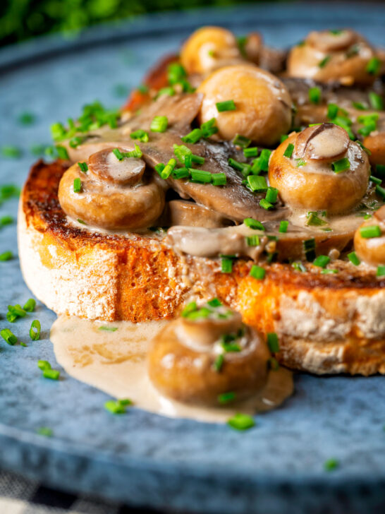 Close-up creamy garlic mushrooms on toast with snipped chives.