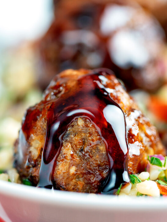 Close-up harissa beef meatballs drizzled with pomegranate molasses served with bulgur wheat.