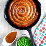 Overhead cooked Cumberland sausage ring with onion gravy, peas and mash.