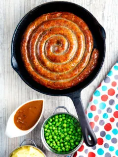 Overhead cooked Cumberland sausage ring with onion gravy, peas and mash.