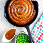 Overhead cooked Cumberland sausage ring with onion gravy, peas and mash featuring a title overlay.