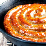 Close up cooked Cumberland sausage ring in a cast iron pan.