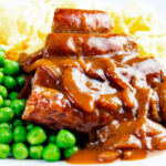 Cooked Cumberland sausage ring with onion gravy, peas and mash.