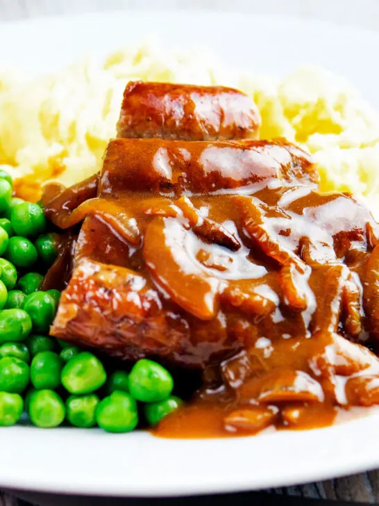 Cooked Cumberland sausage ring with onion gravy, peas and mash.