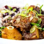 Close-up Jamaican curry goat served with rice and peas featuring a title overlay.
