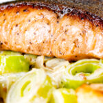 Close up pan fried salmon with crispy skin served with creamed leeks.