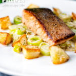 Pan fried salmon fillet with crispy skin served with creamed leeks and parmentier potatoes featuring a title overlay.