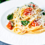 Roasted garlic pasta with tomatoes and spinach garnisheed with parmesan cheese.