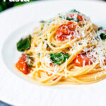 Roasted garlic pasta with tomatoes and spinach garnisheed with parmesan cheese featuring a title overlay.