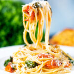 Roasted garlic pasta with tomatoes and spinach being picked up with a fork.