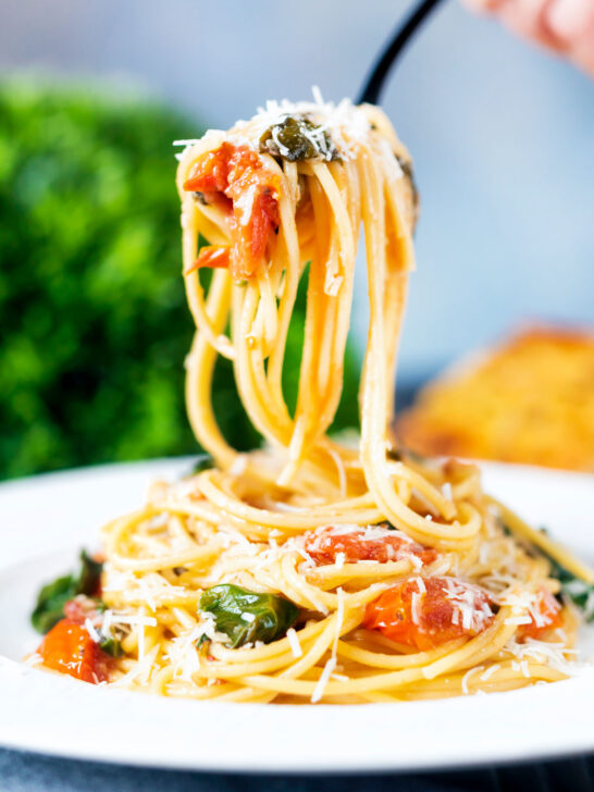 Roasted garlic pasta with tomatoes and spinach being picked up with a fork.