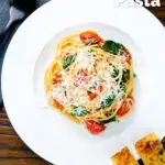 Overhead roasted garlic spaghetti with tomatoes and spinach garnished with parmesan cheese featuring a title overlay.