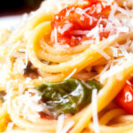 Close-up roasted garlic spaghetti with tomatoes and spinach garnished with parmesan cheese.
