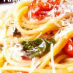 Close-up roasted garlic spaghetti with tomatoes and spinach garnished with parmesan cheese featuring a title overlay.