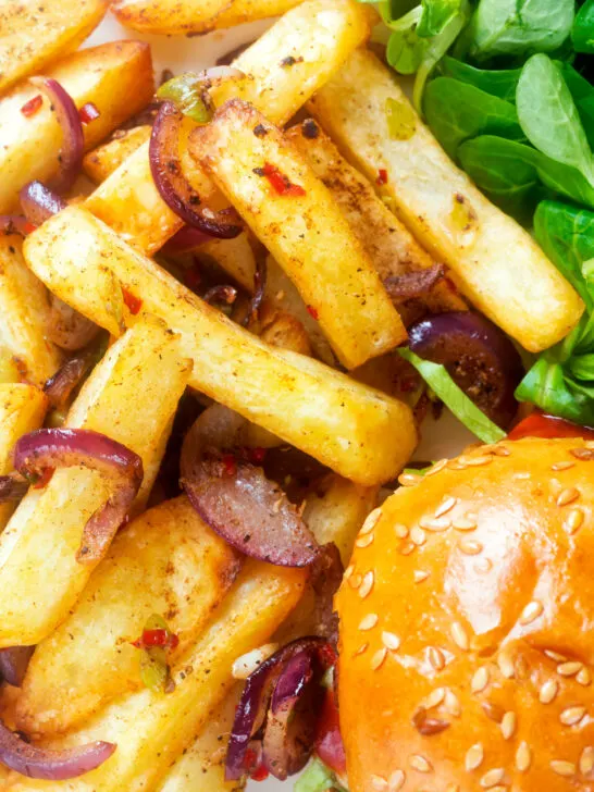 Overhead close-up Chinese takeaway style salt and pepper chips served with a burger.