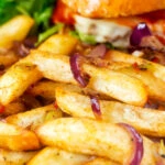 Close-up Chinese takeaway style salt and pepper chips served with a burger.